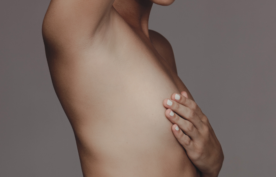 Person i bar överkropp täcker för sitt bröst.